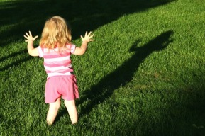 A young girl observes her shadow on the grass.