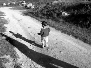 A small boy observes his own shadow while a parent's shadow looks on.