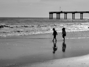 Children walk along the beach at low tide, with shadows.